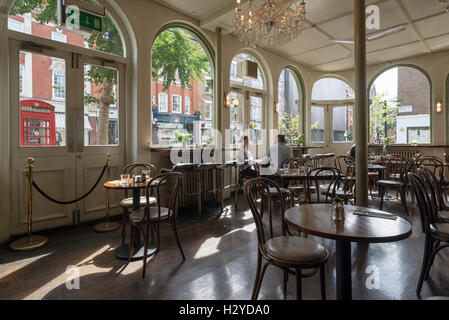 Junges Paar sitzt auf Holzstühlen am runden Tisch zum Frühstück im stilvollen Coco Momo Cafe in Marylebone High Street, Westminster, London, UK Stockfoto