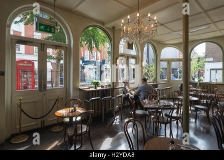 Junges Paar sitzt auf Holzstühlen am runden Tisch zum Frühstück im stilvollen Coco Momo Cafe in Marylebone High Street, Westminster, London, UK Stockfoto