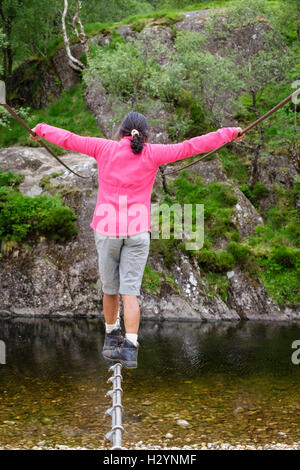 Rückansicht einer Frau Lastausgleich über Steall Drahtseil Brücke über Fluss Nevis zu gehen. Glen Nevis Fort William Schottland Großbritannien Großbritannien Stockfoto