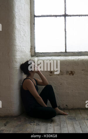 Traurige junge Frau saß auf dem Boden am Fenster Stockfoto