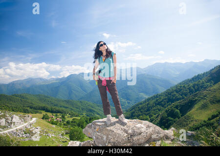 Brünette Sport wandern oder trekking Frau mit braunen grünen Hemd Hose und Sonnenbrille denken Blick auf Tal und Berg Stockfoto