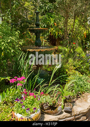 Garten mit reich verzierten Brunnen umgeben von Masse von Smaragd grünes Laub, Bäume & bunte Blumen in dekorativen Behältern Stockfoto