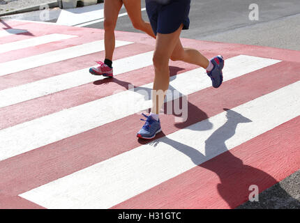 Läufer bei einem Marathonrennen in der Stadt auf einem Fußgängerüberweg mit roten und weißen Streifen Stockfoto