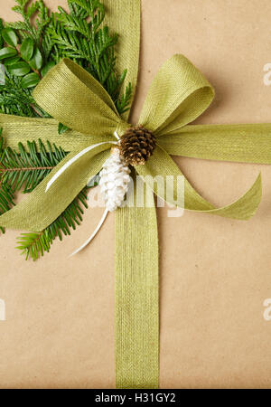 Nahaufnahme von Bogen und natürliche immergrünen Dekorationen auf Weihnachtsgeschenk. Weihnachtsgeschenk in Recycling-Geschenkpapier eingewickelt. Stockfoto