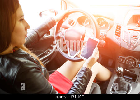 Junge Frau im roten Kleid im Auto zu sitzen und halten smartphone Stockfoto