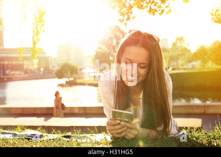 lustiges Mädchen mit einem Smartphone auf dem Rasen eines Parks mit einem grünen Hintergrund Stockfoto