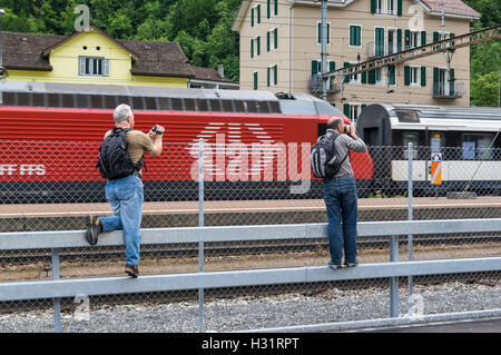 Amateure, die Videos und Bilder von einem vorbeifahrenden Zug mit einem roten Lok mit dem Logo der Schweizerischen Bundesbahnen SBB. Erstfeld, Schweiz. Stockfoto