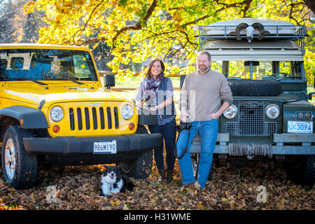 Ein Mann und Frau stand vor einem Jeep Wrangler und Land Rover mit einem Border Collie. Stockfoto
