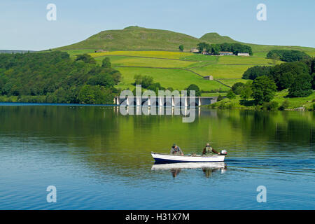 Fischer im Boot auf ruhige blaue Wasser des Sees Ladybower, Ashopton Viadukt & Ackerland im Hintergrund unter blauem Himmel in England Stockfoto