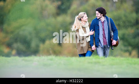 Junge Paare, die zusammen an einem regnerischen Tag. Sie sind Hand in Hand und sprechen. Stockfoto