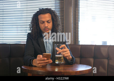 Junger Mann mit seinem Smartphone, während Sie ein Bier in einer Bar genießen. Stockfoto