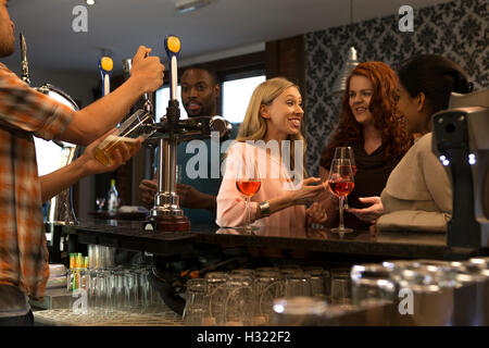 Gruppe von Personen in einem Pub genießen Sie Getränke und reden. Ein Barkeeper kann gesehen werden, ein Bier in Strömen. Stockfoto