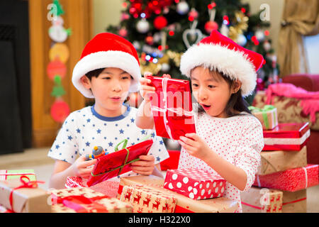 Chinesische Geschwister zusammen auf dem Boden in ihrem Wohnzimmer sitzen am Weihnachtsmorgen. Sie sind Öffnung Geschenke mit aufgeregt Stockfoto