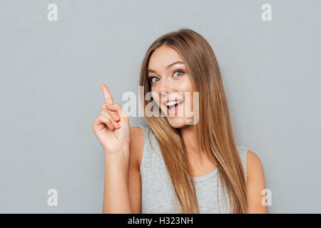 Glückliche junge Frau deutete Finger oben auf Exemplar auf einem grauen Hintergrund isoliert Stockfoto