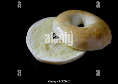 Ein Bagel, der in zwei Hälften geschnitten und mit Butter auf einem schwarzen Hintergrund wurde Stockfoto