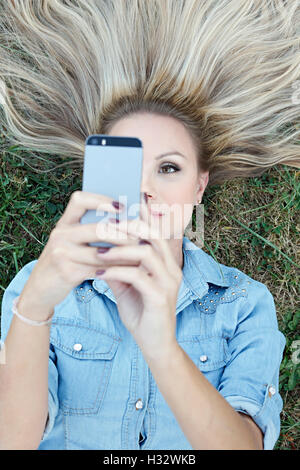 Schöne junge blonde liegen auf dem Rasen und unter selfie Stockfoto