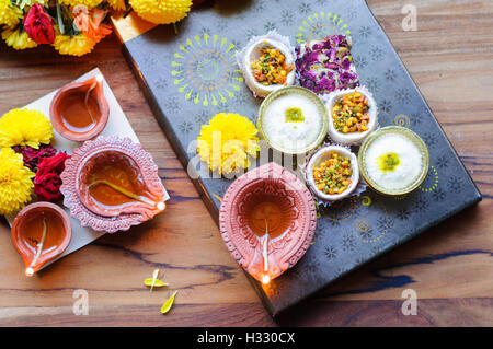 Diya Lampen angezündet während Diwali-fest mit Blumen und Süßigkeiten im Hintergrund Stockfoto