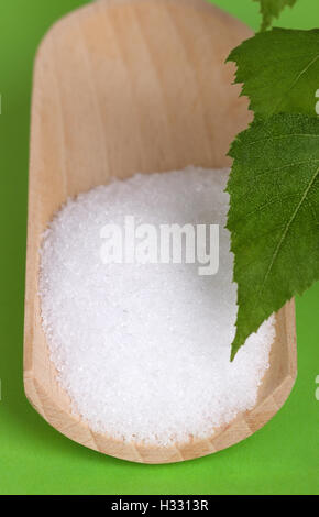 Xylitol Birkenzucker auf hölzerne Schaufel mit Birke Blätter über grün. Weißer granulierter Zuckeralkohol, Ersatz als Süßstoff verwendet. Stockfoto