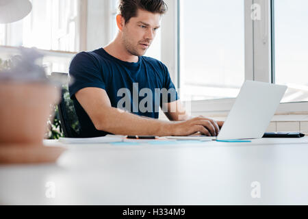 Voll junger Mann auf Laptop-Computer im Büro arbeiten. Junge männliche Führungskraft mit Laptop an seinem Schreibtisch. Stockfoto