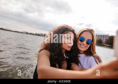 Schuss von schönen Mädchen, die die Selfie mit Handy am See. Junge Frauen posieren für Selbstporträt. Stockfoto