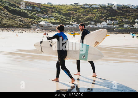 Zwei junge Männer tragen die Bretter an den Strand nach dem Surfen Sennen Cove, Cornwall Stockfoto