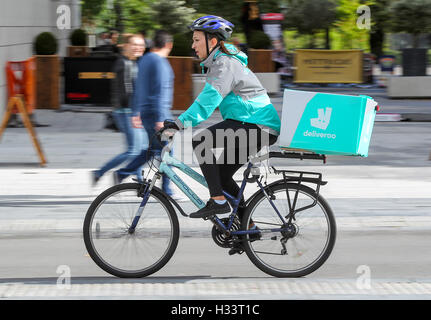 Eine weibliche Deliveroo Radsportler mit einem Paket auf ihrem Fahrrad Stockfoto