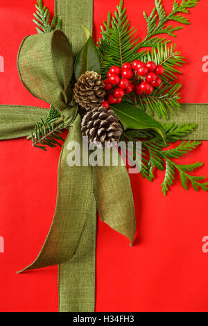 Nahaufnahme eines klassischen roten und grünen Weihnachts-Geschenk Weihnachtsgeschenk mit Stoff Schleife und immergrüne botanische Dekorationen Stockfoto