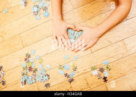 kleines Kind mit Rätseln auf Holzboden zusammen mit Eltern, Lifestyle-Menschen-Konzept, liebevollen Händen miteinander spielen Stockfoto