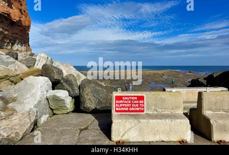 Vorsicht Zeichen Oberfläche kann durch marine Bewuchs rutschig sein. Staithes North Yorkshire England UK Stockfoto