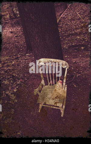 Ein Vintage Kind Schaukelstuhl sitzt mitten im Wald. Eine alte Puppe sitzt auf dem Stuhl. Stockfoto