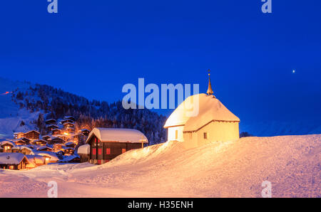 Blaue Dämmerung auf der alpinen Dorf und Kirche bedeckt mit Schnee, Bettmeralp, Bezirk Raron, Kanton Wallis, Schweiz Stockfoto