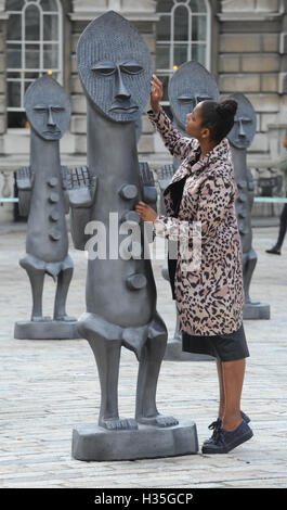 Eine Frau schaut einer der lebensgroßen Armee von 40 maskierte afrikanische Figuren auf dem Display in der Edmond J Safra Brunnen Hof des Somerset House, central London, starten die die 01:54 Messe für zeitgenössische afrikanische Kunst. Stockfoto