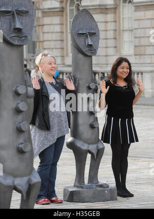 Zwei Frau Pose mit einer der lebensgroßen Armee von 40 maskiert afrikanische Figuren auf dem Display in der Edmond J Safra Brunnen Hof des Somerset House, central London, starten die die 01:54 Messe für zeitgenössische afrikanische Kunst. Stockfoto