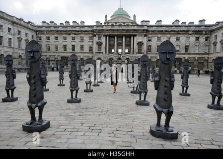 Eine Frau geht zwischen die lebensgroße Armee von 40 maskierte afrikanische Figuren auf dem Display in der Edmond J Safra Brunnen Hof des Somerset House, central London, starten die die 01:54 Messe für zeitgenössische afrikanische Kunst. Stockfoto