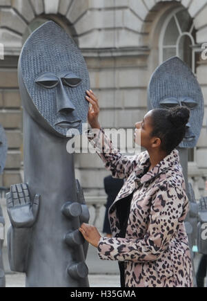 Eine Frau schaut einer der lebensgroßen Armee von 40 maskierte afrikanische Figuren auf dem Display in der Edmond J Safra Brunnen Hof des Somerset House, central London, starten die die 01:54 Messe für zeitgenössische afrikanische Kunst. Stockfoto