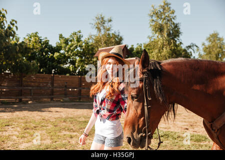 Fröhliche junge Frau Cowgirl halten und walking wit ihr Pferd auf der ranch Stockfoto