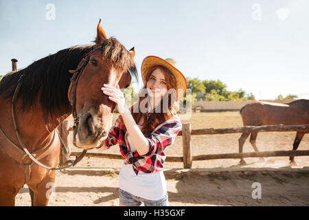 Gerne schöne junge Frau Cowgirl Hut kümmert sich um ihr Pferd auf der ranch Stockfoto