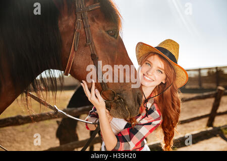 Attraktive junge Frau Cowgirl mit ihrem Pferd auf Hof stand lächelnd Stockfoto