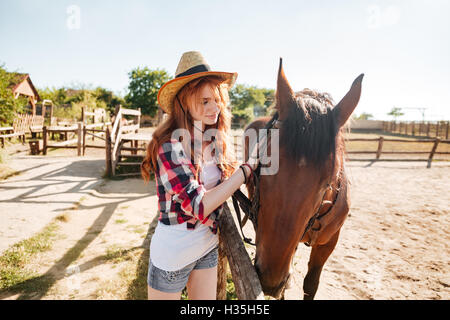 Schöne rothaarige junge Frau Cowgirl Hut kümmert sich um ihr Pferd auf Bauernhof Stockfoto