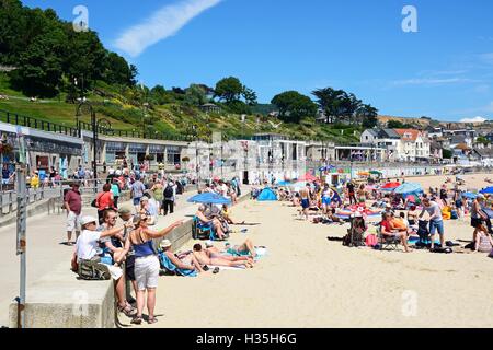 Urlauber entspannen auf dem sandigen Strand mit der Promenade nach hinten, Lyme Regis, Dorset, England, Vereinigtes Königreich, West-Europa. Stockfoto