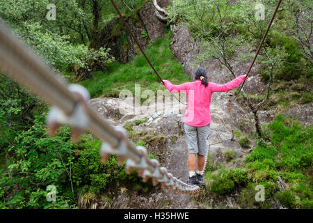 Asiatische Frau in rosa zu Fuß über Steall Drahtseil Brücke über Wasser von Nevis River. Glen Nevis Fort William Highland Schottland UK Großbritannien Stockfoto