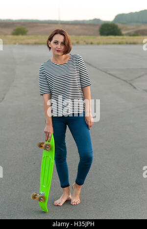 Mädchen stehen barfuß auf dem Asphalt mit einem Skateboard. Stockfoto