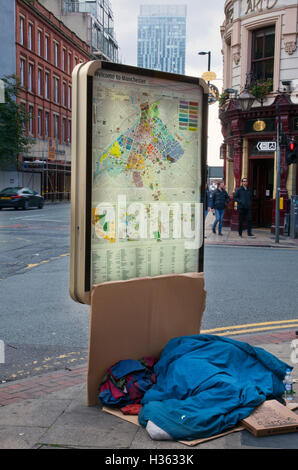 Wohnungslosigkeit, Menschen & Passanten vorbei behandelt obdachlose Bettler, Schlafen auf dem Gehsteig gegen einen Stadtplan Reklametafeln, geben einige Unterkünfte, auf den Straßen von Manchester, UK. Stockfoto