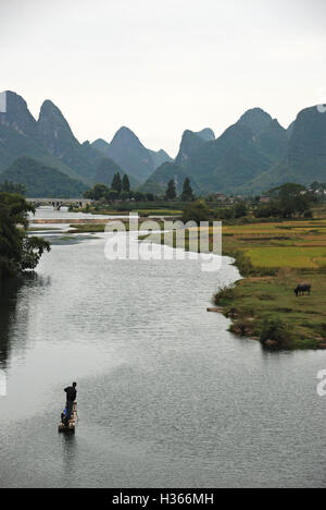 Ein Fischer steht auf seinem Bambusfloß, wie er auf dem idyllischen Yulong Fluss in Guangxi, China Paddel. Stockfoto