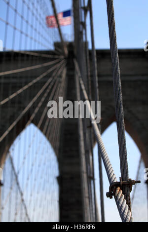 Tragseile auf der Brooklyn Bridge mit amerikanischer Flagge am Brückenturm im Hintergrund. New York City, USA Stockfoto