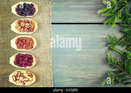 Retro getönten Weihnachten Snacks Hintergrund, Fichte Zweige, getrockneten Früchten und Nüssen in Holzschalen auf Leinen und Holz Hintergrund. Stockfoto