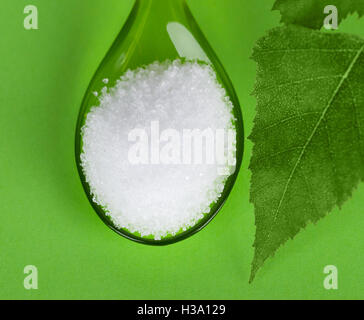 Xylitol Birkenzucker auf Plastiklöffel mit Birke Blätter auf grünem Hintergrund. Weißen granulierten Zucker-Alkohol-Ersatz. Stockfoto