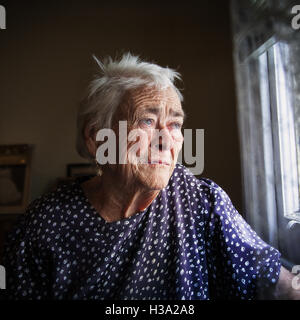 Alte Frau am Fenster sitzen draußen blicken. Sie sieht in ihren tiefen, einsamen Gedanken traurig. Stockfoto