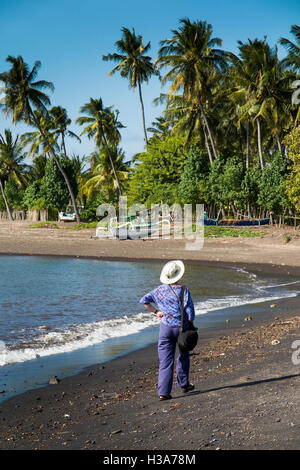 Indonesien, Lombok, Selengan, Fischerdorf, Touristen zu Fuß auf schwarzen vulkanischen Sand Strand Stockfoto