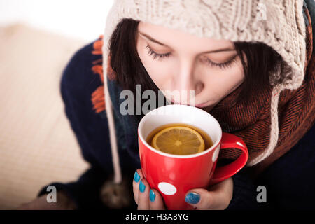 Frau eine große Tasse frisch gebrühtem Tee genießen, wie sie auf dem Sofa im Wohnzimmer entspannt Stockfoto